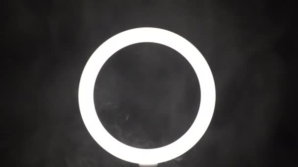 A stream of smoke in front of a ring of light from a led lamp on a black background close-up. The vaper blows steam in the frame. The concept of a dance club and a stage with spotlights — Wideo stockowe