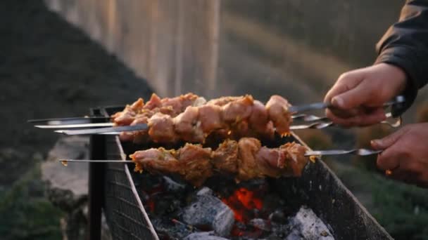Een man kookt barbecue op spies op houtskool grill op straat. Barbecue buiten. Picknick in de natuur. Zet spiesen met vlees op de grill — Stockvideo
