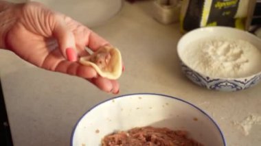 Bir kadın hamur köftelerini kendi elleriyle yontuyor ve bir ev mutfağında kıyma yapıyor. Ev yapımı yemekler.