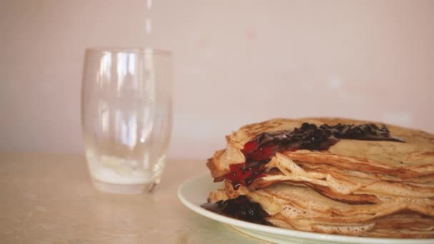 La confitura del primer plano fluye sobre la pila de los crepes frescos. La leche se vierte en una taza. Comida casera en un plato. bollería dulce — Vídeos de Stock