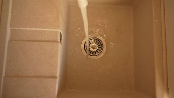 El agua vierte de un grifo en un fregadero de cocina y drena en un primer plano de desagüe. Consumo de agua potable limpia. Trabajos domésticos — Vídeos de Stock