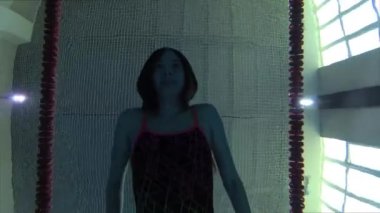 Eşofmanlı, dalış gözlüklü, mayo takan kadın yüzücü havuzda antrenman yapıyor. Sporcu su altında yüzer. Sualtı çekimi, geniş açı, 4K.