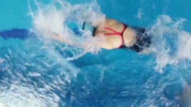 Eşofmanlı, dalış gözlüklü, mayo takan kadın yüzücü havuzda antrenman yapıyor. Sporcu kelebek stilinde yüzer. Geniş açı, 4k..