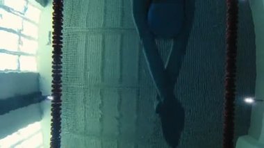 Eşofmanlı, dalış gözlüklü, mayo takan kadın yüzücü havuzda antrenman yapıyor. Sporcu su altında yüzer. Sualtı çekimi, geniş açı, 4K.