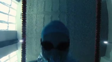 Eşofmanlı, dalış gözlüklü, mayo takan kadın yüzücü havuzda antrenman yapıyor. Sporcu su altında yüzer. Sualtı çekimi, geniş açı, 4K.