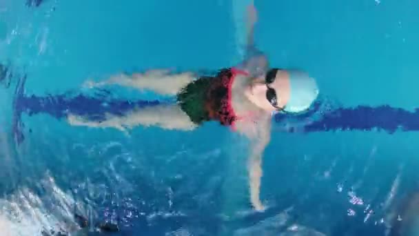 身穿运动服 戴着潜水护目镜 戴着泳帽的女运动员正在游泳池里训练 运动员背着她游了进来 — 图库视频影像