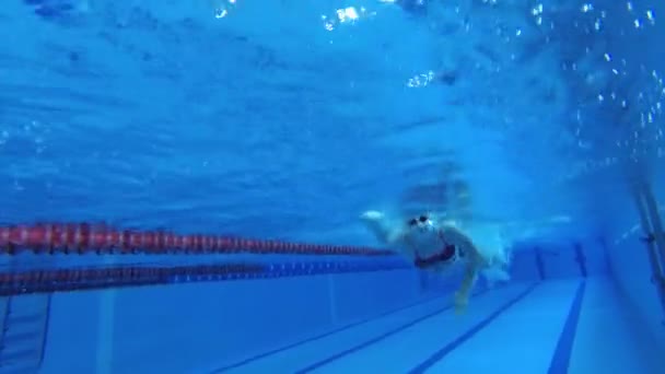 身穿运动服 戴着潜水护目镜 戴着泳帽的女运动员正在游泳池里训练 运动员在水下游泳 水下射击 — 图库视频影像