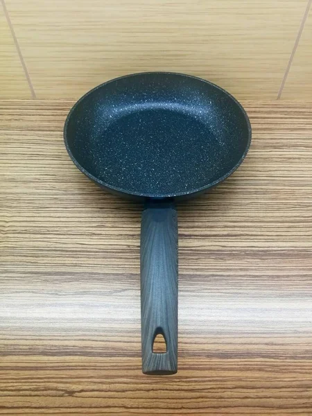 Black aluminum pan with black plastic handle, placed on the kitchen counter, view from the handle, image