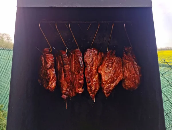 Meat smoked in a tin smoker, six pieces of meat prepared on steel hooks, image