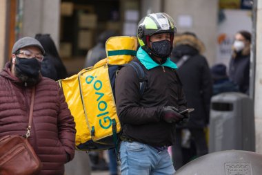 Madrid, İspanya - 27 Aralık 2020: Glovo şirketinden bir yemek teslimatçısı, binici, işini yapmak için cep telefonunu kullanıyor