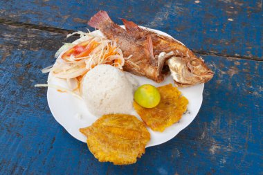 Cartagena de Indias, Colombia - Nov 22, 2010: A delicious plate of food, fried fish, rice, fried banana, lime and onion and tomato garnish, on the beach of Isla Baru, in the Colombian Caribbean clipart