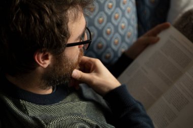 Akşam yemeğinden sonra evdeki kanepede uzanmış kitap okuyan ve okuyan genç bir adam.