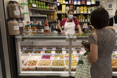 Zaragoza, İspanya - 12 Ağustos 2021: Mercado merkez Zaragoza veya Lanuza pazarında turşu satan bir mağazada çalışan bir kadın, bir müşteriyi gözlemliyor.