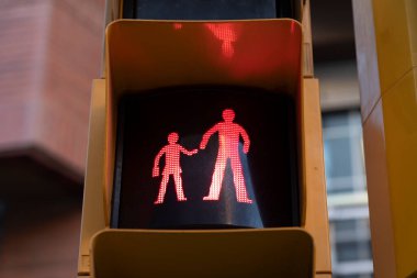 Kırmızı bir trafik ışığı, bir okul bölgesindeki yaya geçidinde durduğunu ve bir çocuğun ve bir yetişkinin el ele tutuştuğunu gösteriyor.