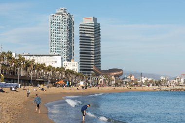 Barselona, İspanya - Ocak 08, 2022: Kışın Barceloneta plajı, plajda eğlenen çok sayıda insan ve arka plandaki karakteristik gökdelenler ve binalar