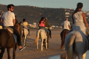 Zahara de los Atunes, Spain - Sept 09, 2021: A group of people, tourists, enjoy an organized horseback ride, along the seashore, on the beach, on a summer afternoon