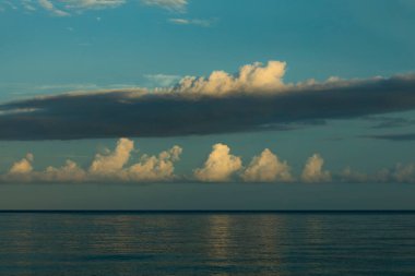 Bulutlar suyu yansıtıyor ve günün son ışıklarıyla aydınlanıyor, denizin üzerinde ve sessiz ufuk çizgisinde, Raja Ampat Adaları, Batı Papua, Endonezya