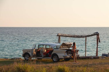 Playa Giron, Küba - Nisan. 03, 2010: Genç bir kız Karayip Denizi kıyısında park edilmiş eski bir Küba arabasının bagajında bir şey arıyor