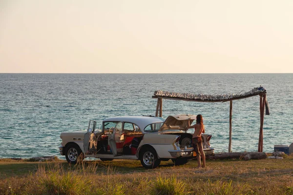 Playa Giron, Küba - Nisan. 03, 2010: Genç bir kız Karayip Denizi kıyısında park edilmiş eski bir Küba arabasının bagajında bir şey arıyor