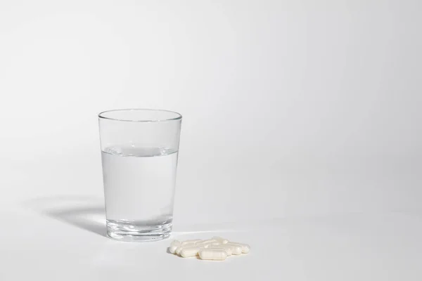 Glass of water isolated with medicine pills on white background, real photo studio, no 3D