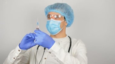 Genç ve yakışıklı bir doktor aşıya hazırlanır, enjeksiyondan önce aşıyla bir şırınga hazırlar. Doktorun elleri şırıngayı aşıyla doldurur ve enjeksiyona hazırlanır.