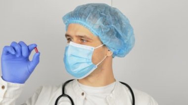 Tıbbi maskeli genç bir doktor elinde yeni bir ilaç sunan kırmızı bir hap tutuyor. Genç bir doktor sunumda yeni bir ilaç gösteriyor, tüm hastalıklar için kırmızı bir hap..