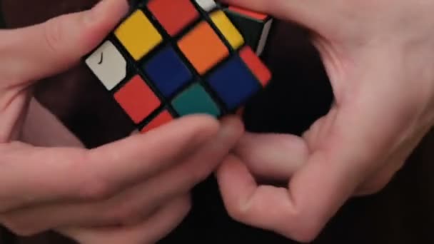 Primer plano de una mano de hombre joven, trata de resolver un cubo de Rubiks. Un joven atractivo recoge un cubo de Rubiks. Un joven resuelve un rompecabezas, entrena para recoger un cubo de Rubiks. — Vídeo de stock