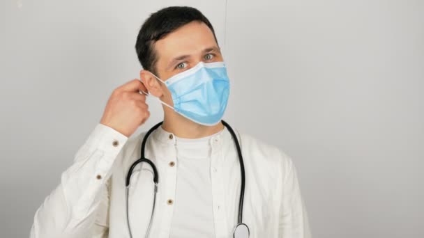 Młody przystojny lekarz zdejmuje swoją medyczną maskę ochronną i ciężko wzdycha.. — Wideo stockowe