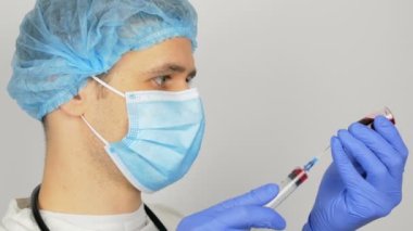 Genç yakışıklı doktor Covid-19 aşısı için hazırlanıyor, iğneden önce aşıyla birlikte bir şırınga hazırlıyor. Doktor bir şırıngayı kırmızı aşıyla doldurur ve bir hastaya enjekte etmeye hazırlanır..