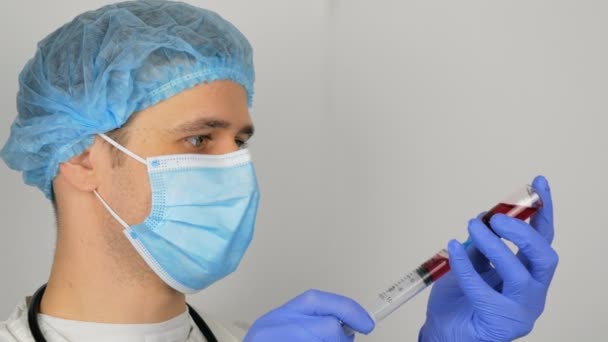 El joven y guapo médico se prepara para la vacunación con Covid-19, prepara una jeringa con una vacuna antes de la inyección. El médico llena una jeringa con una vacuna roja, preparándose para inyectar a un paciente.. — Vídeos de Stock