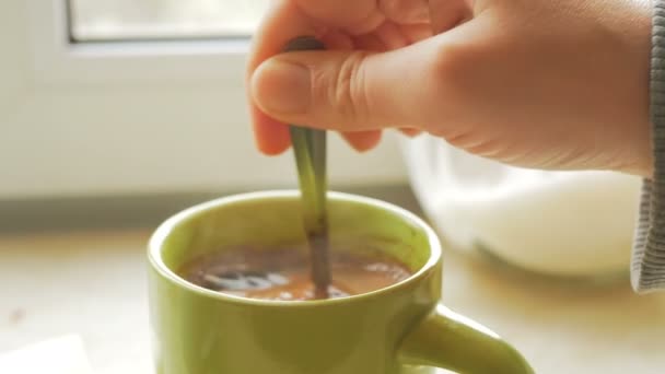 Крупним планом молода приваблива жіноча рука вона перемішує цукор в чашку з ароматною натуральною кавою. Ароматна свіжозварена кава в зеленій чашці знаходиться на кухонному столі. — стокове відео
