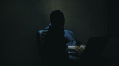Siyah kapüşonlu bir bilgisayar korsanı şifreleri kırıp önemli internet kullanıcı veritabanlarını indiriyor. Siyah kar maskeli bir internet korsanı sandalyeye oturur ve laptoptan veri çalar.