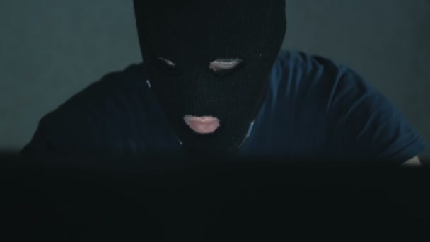 Een anonieme hacker in een zwarte hoodie belt zijn slachtoffer aan de telefoon en dreigt de database wachtwoorden te kraken. Een internet hacker in een zwarte bivakmuts zit in een stoel en steelt data van een laptop — Stockvideo