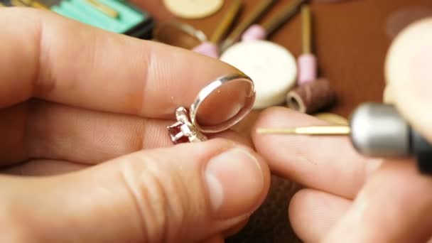 Ein Juwelier schneidet einen Edelstein auf einen Goldring. Ein professioneller Juwelier poliert mit einem Spezialwerkzeug einen roten Stein auf einem Goldring. Schmuckverarbeitung, Edelsteinpolieren durch einen professionellen Juwelier. — Stockvideo