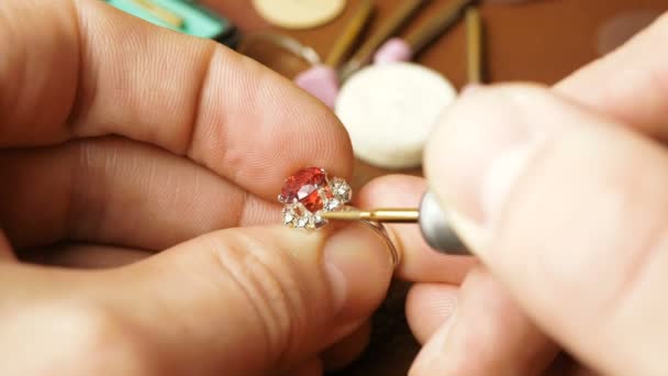 A jeweler is cutting a precious stone on a gold ring. A professional jeweler polishes a red stone on a gold ring using a special tool. Jewelry processing, gemstone polishing by a professional jeweler. — Stock Video