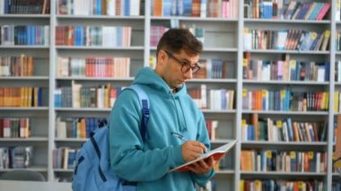 Kitabevinin arka planında halk kütüphanesinde duran genç bir öğrenci defterine bir şeyler yazıyor. Arka planda genç ve çekici bir öğrencinin yakın plan portresi.