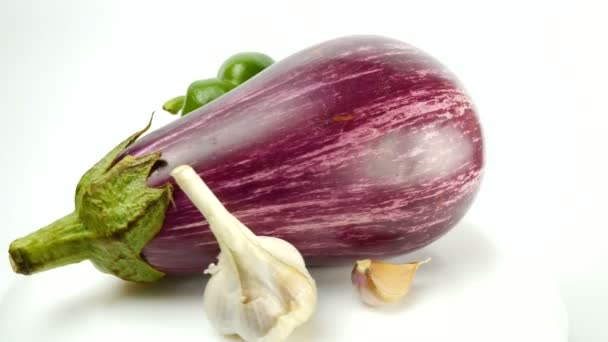 L'aubergine, le poivron, la tomate, l'ail et l'œuf de caille reposent sur une assiette et tournent sur un fond blanc. Concept d'aliments sains.Légumes biologiques juteux frais tournent sur une assiette blanche. — Video