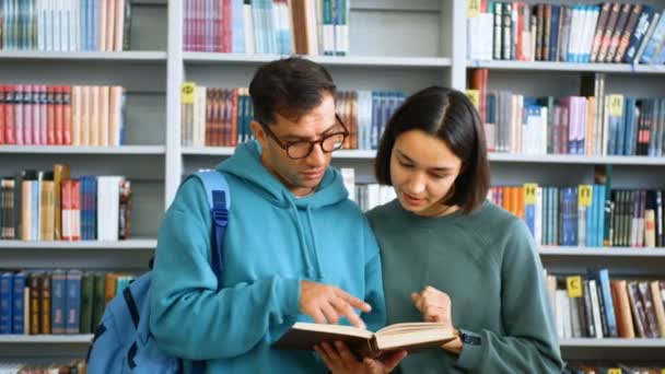 Close-up portret van een jonge aantrekkelijke jongen student en een jonge vrolijke vrouw student, ze zijn op zoek naar de nodige informatie in een boek, de voorbereiding van een les op de achtergrond van — Stockvideo