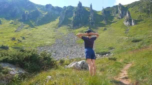 若い魅力的な女性旅行者が山のふもとに立って、彼女の腕が側面に伸びている距離を見ています。 — ストック動画