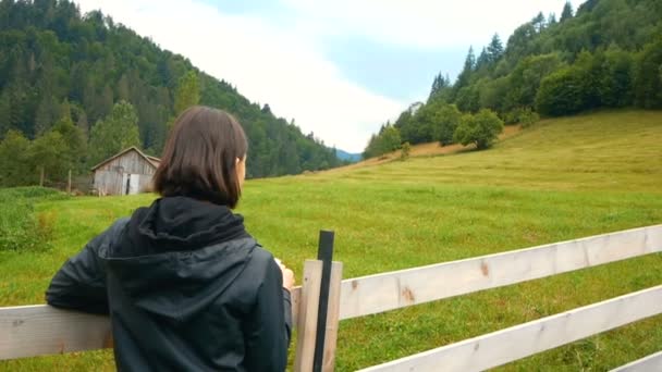 Young attractive woman farmer drinks coffee while standing near the wooden fence of her ranch. — Stock Video