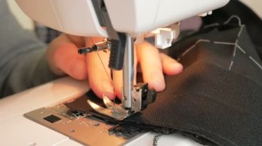 İlgili genç bir ev hanımı dikiş makinesi kullanarak koruyucu maskeler dikiyor. Karantina sırasında genç ve çekici bir kadın gönüllüyü yakından çekerek tıbbi koruyucu maskeler dikiyor. Şunun yakın çekimi: