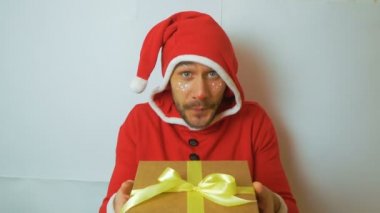 Kırmızı Santaclaus karnaval kostümü giymiş genç yakışıklı bir adam Noel 'i kutlamak için bir hediye veriyor. Noel elf kostümü giymiş genç bir adam gülümseyip selamlaşırken elini sallıyor.