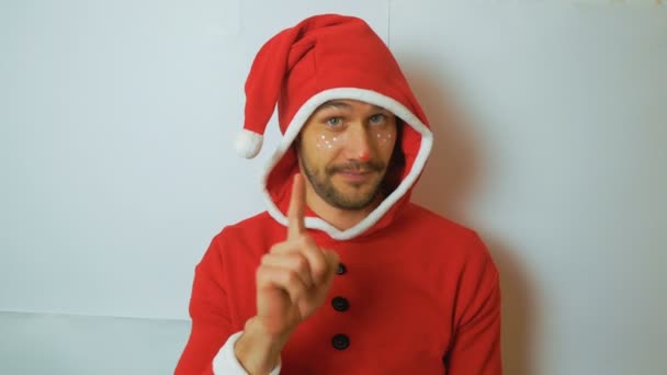 A young handsome guy in a red santaclaus carnival costume holds out a New Years gift congratulating on the holidays.A young funny guy in a Christmas elf costume smiles and waves his hand in greeting — Stock Video