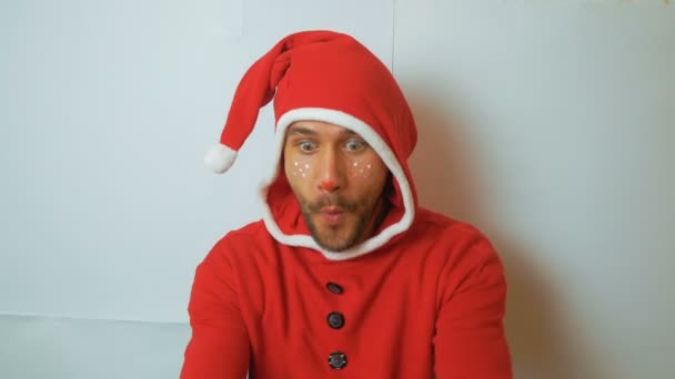 A young attractive funny guy in a New Years costume as Santas assistant receives a New Years gift and rejoices at it. A young funny guy in a New Years elf costume, smiling and waving his hand in — Stockvideo