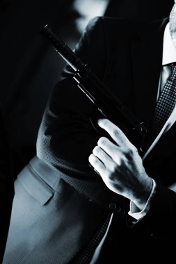 İyi giyimli erkek ajan ajan ajan ajan. Takım elbiseli ve kravatlı. Elinde otomatik tabanca var..