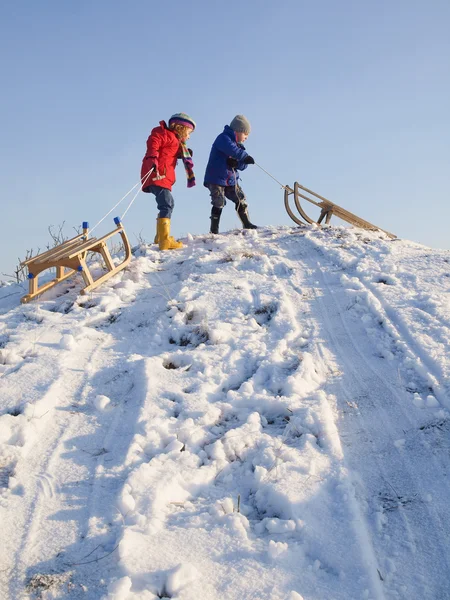 小儿童冬季服装用雪橇顶部的雪盖山 — 图库照片