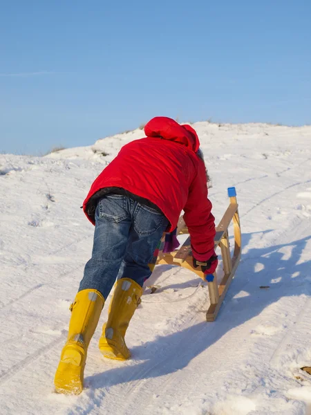 Klein meisje in de winterkleren duwt een slee naar de top van een sn — Stockfoto