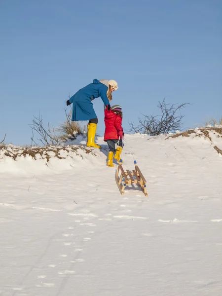 母亲帮助拉雪橇的小女孩 — 图库照片