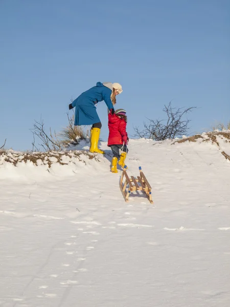 Moeder helpt kleine meisje trekken een slee — Stockfoto