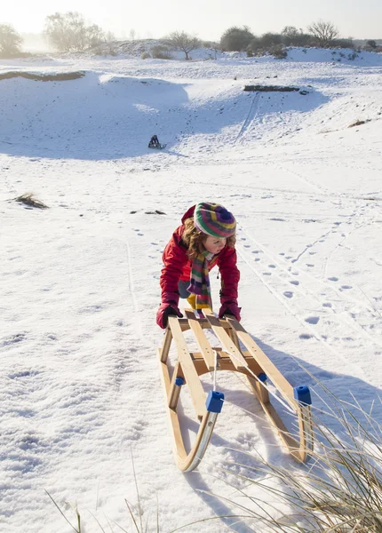 Girl pushing wooden sledge up a hill — Stock Photo, Image